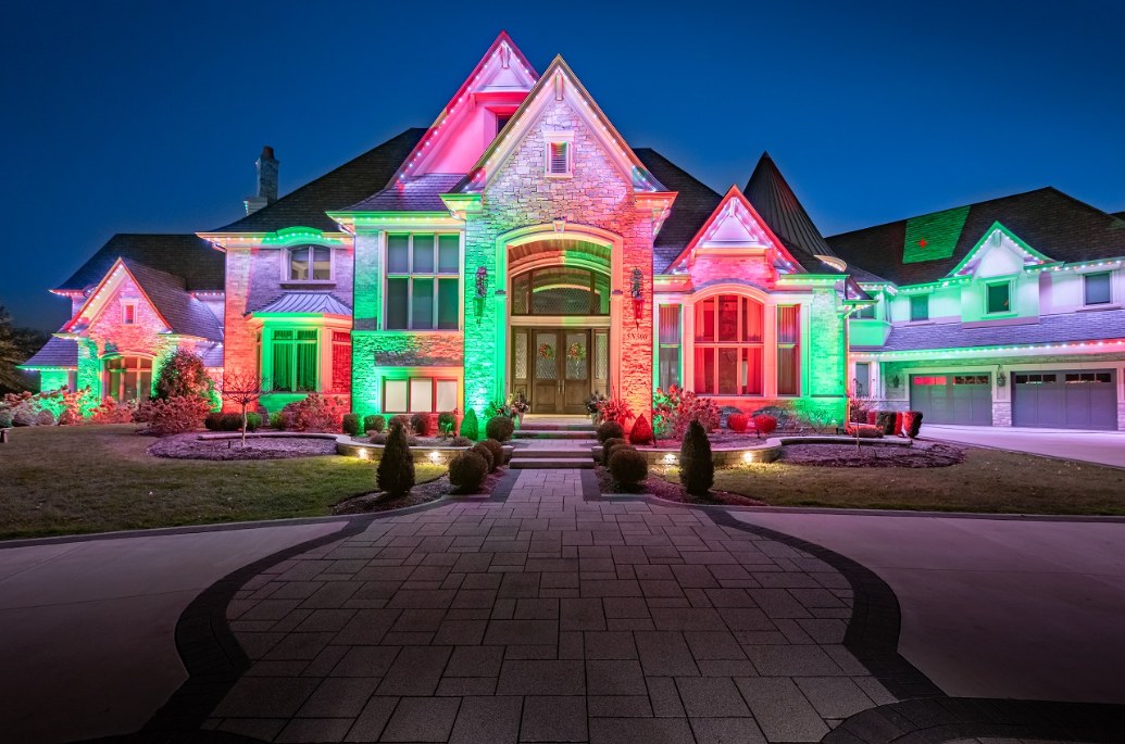 A large stone home lit with red, green and blue holiday lights at dusk